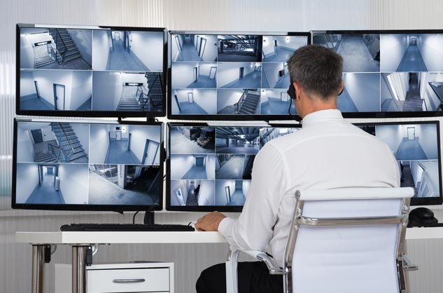 a man sitting at a desk in front of three monitors. cctv solutions